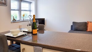 Una cocina moderna con encimera de granito, una botella de Veuve Clicquot, una copa de vino y un comedor con sofá y televisor.