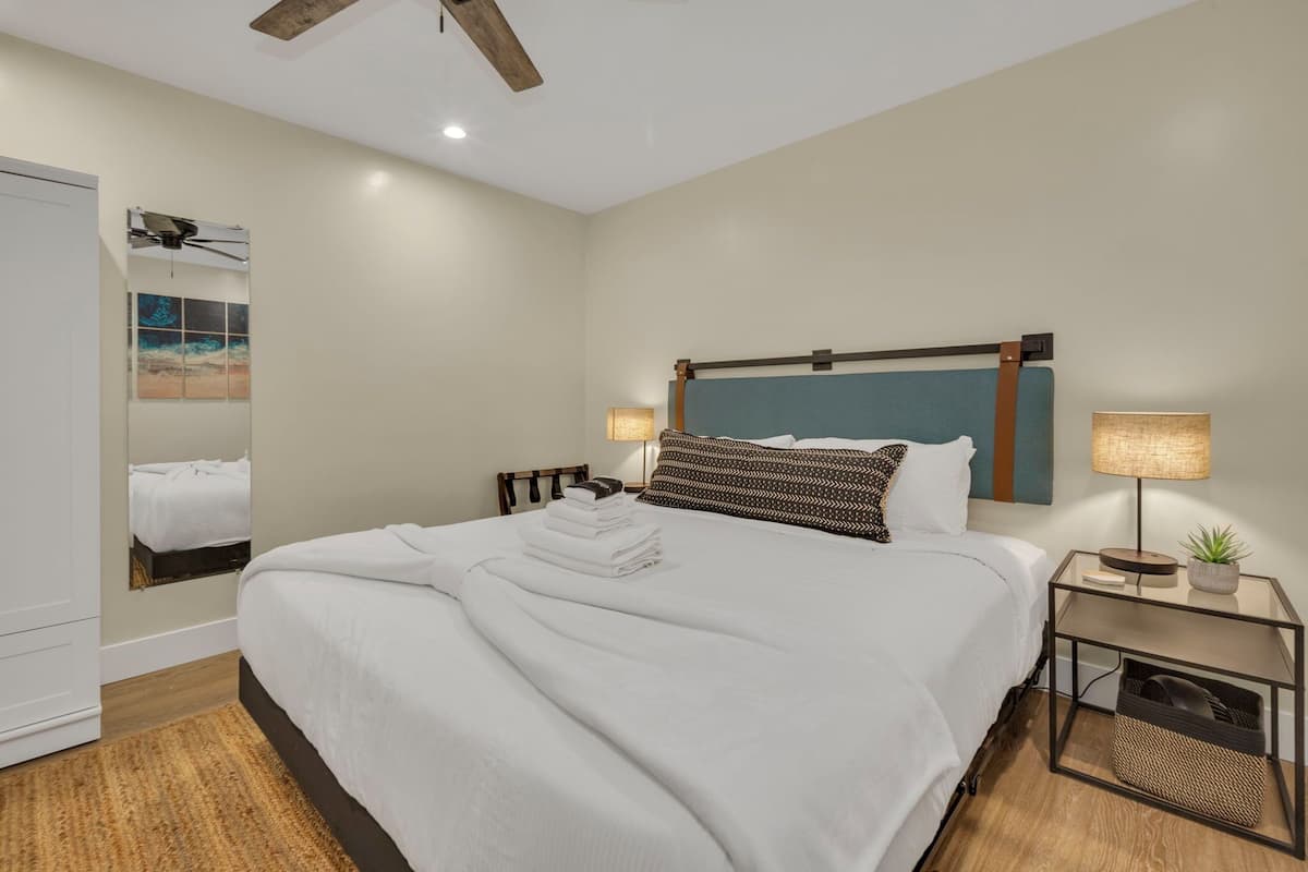 A neatly made bed with white linens, a bedside table with a lamp, and a small plant.
