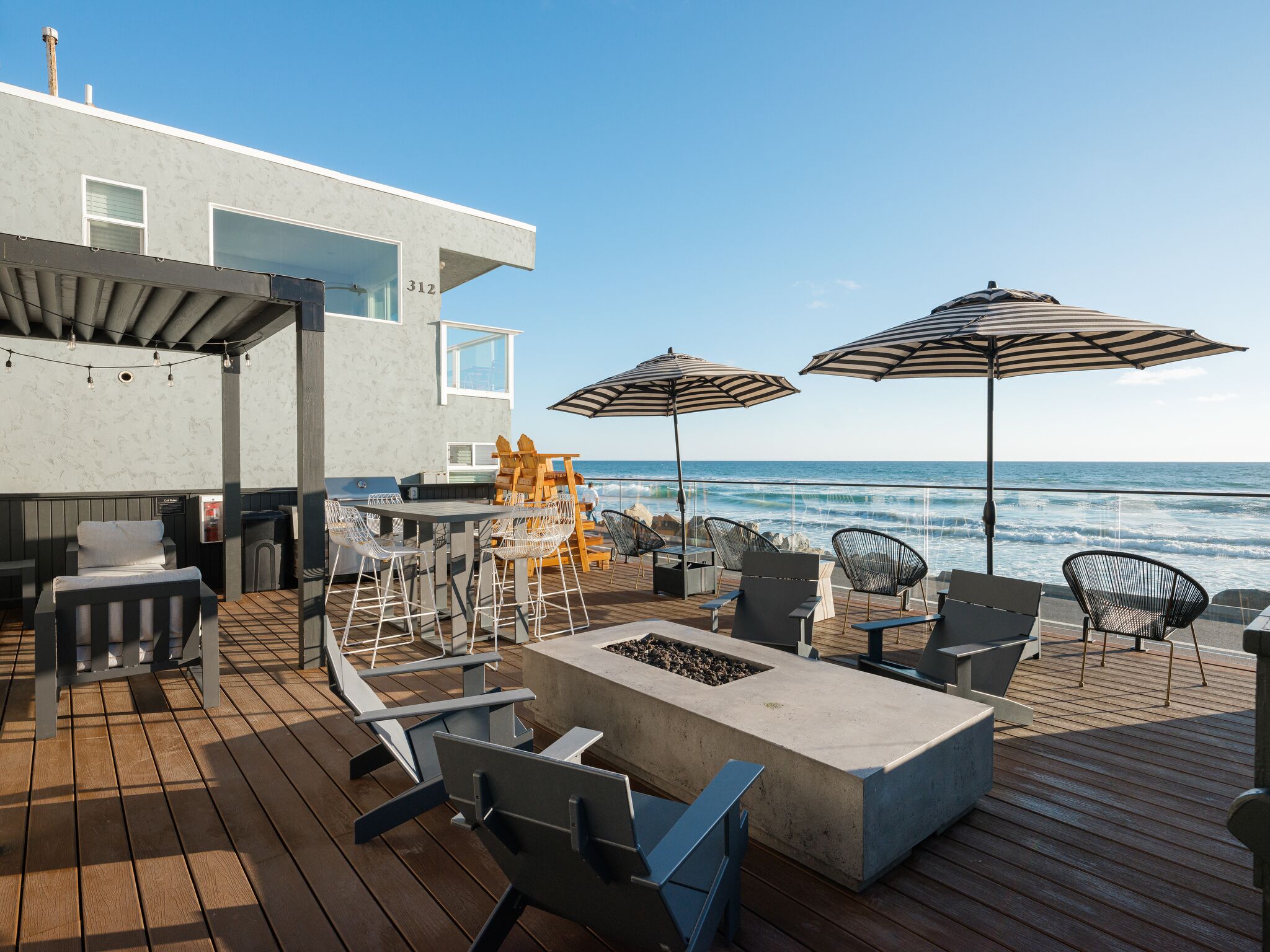 A deck with outdoor seating, a grill, and a view of the ocean.