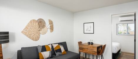 Ein modernes Wohnzimmer mit einem grauen Sofa, einem Couchtisch und einem Essbereich mit einem Holztisch und Stühlen.