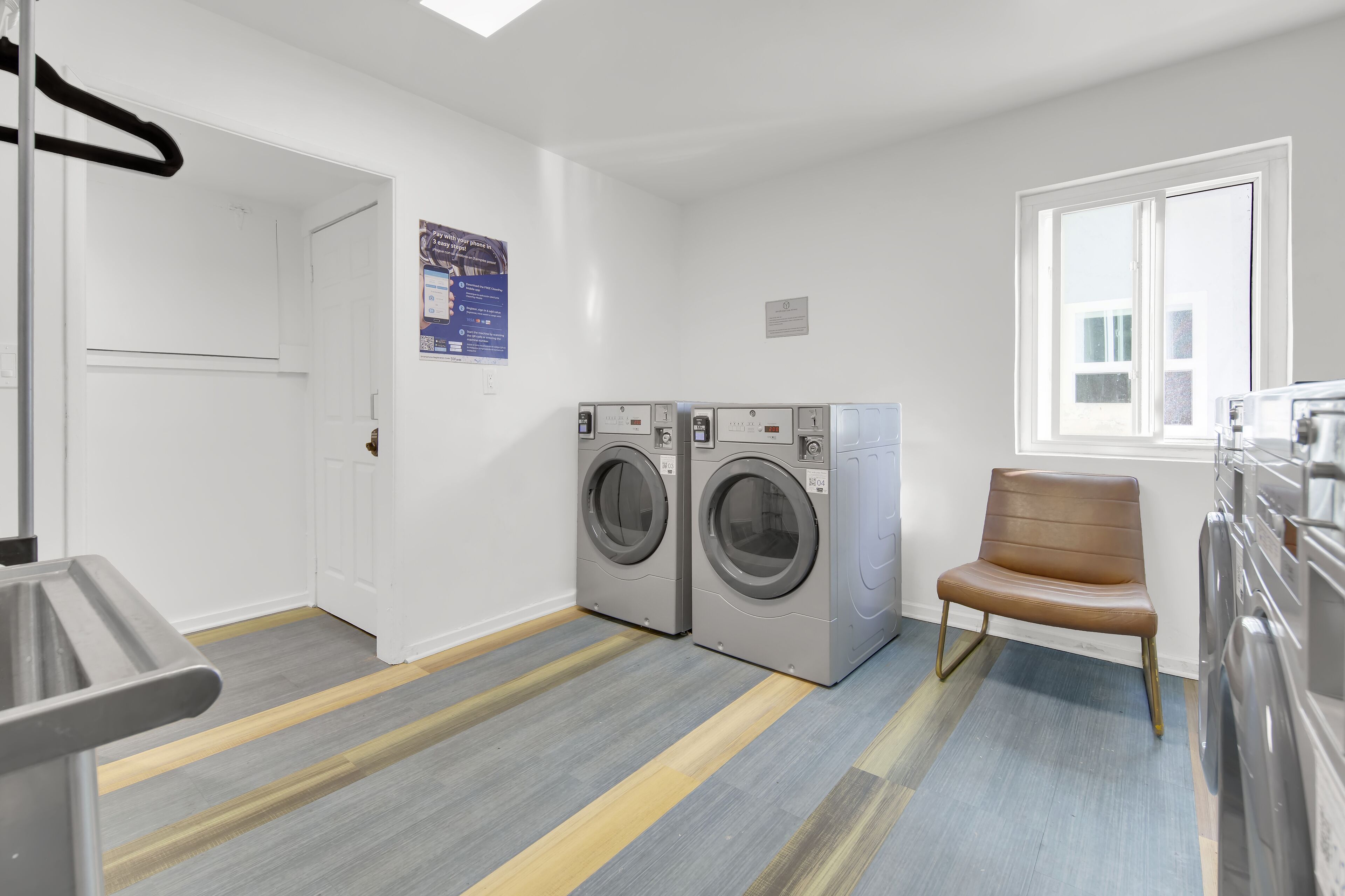 A laundry room with two front-loading washing machines, a chair, and a window.