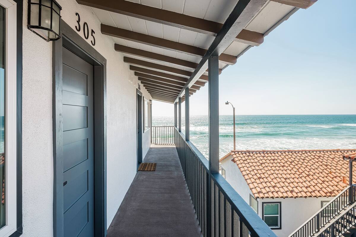 A balcony with a view of the ocean, a door labeled '305', and a tiled roof in the background.
