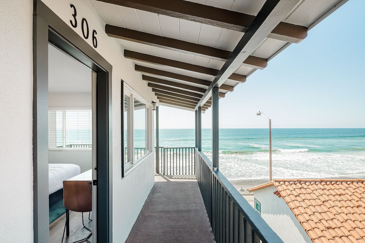 A balcony with a view of the ocean, a bed, and a chair.