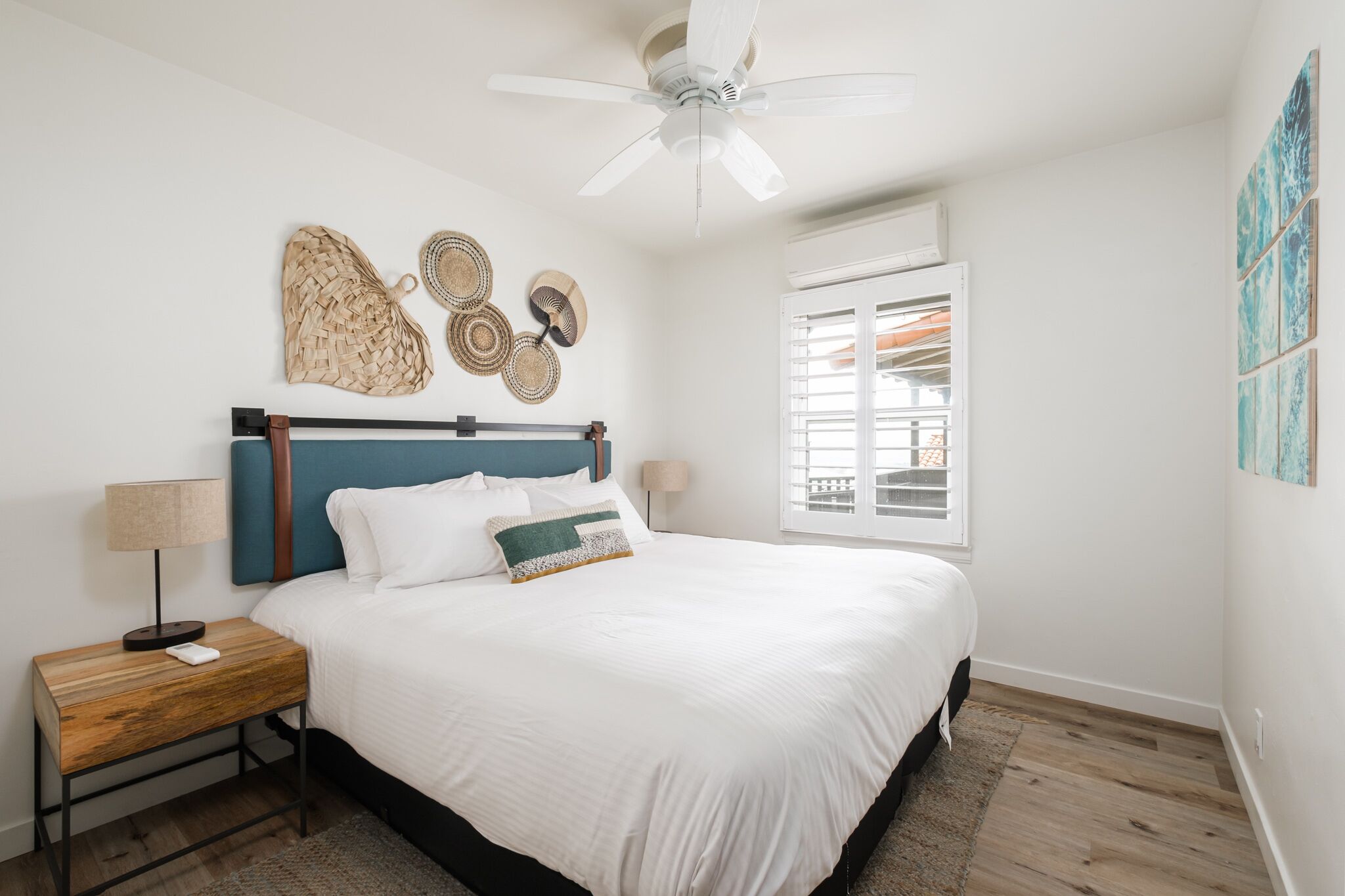 A bedroom with a bed, a nightstand, a ceiling fan, a window with blinds, and wall art.