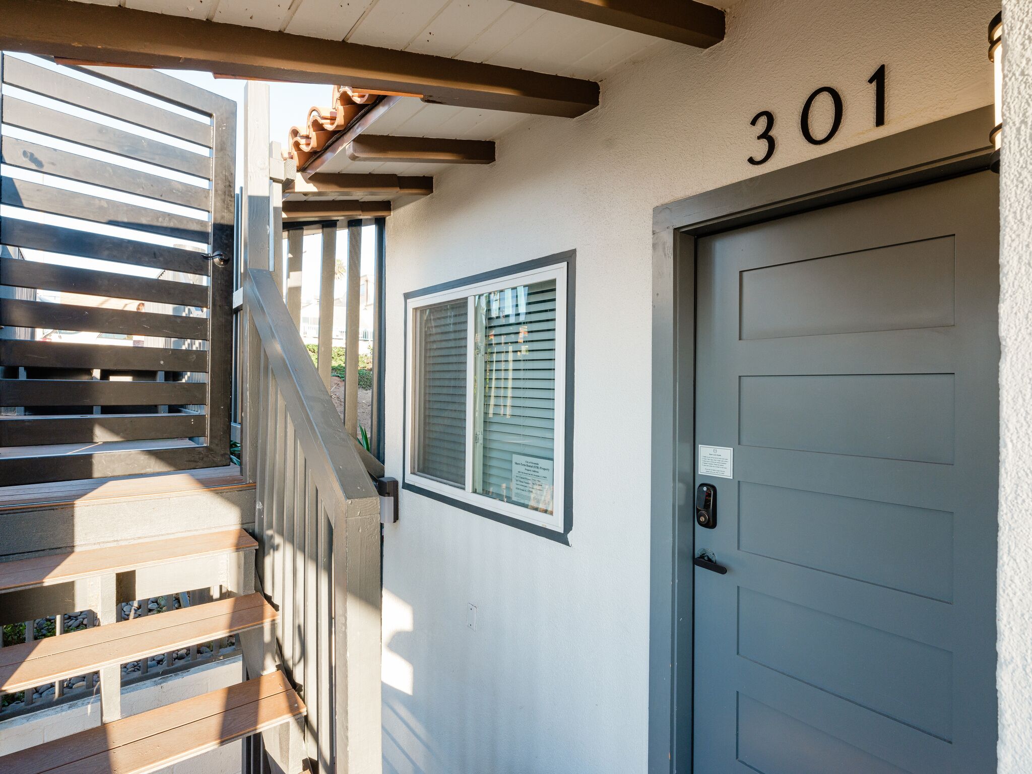 A building entrance with a wooden staircase, a door marked with the number 301, and a window with blinds.