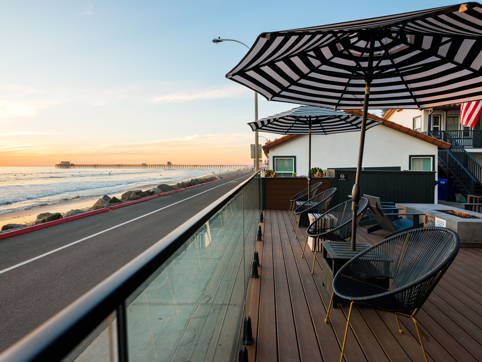 Une terrasse avec des sièges extérieurs, une vue sur l’océan et une jetée visible au loin.