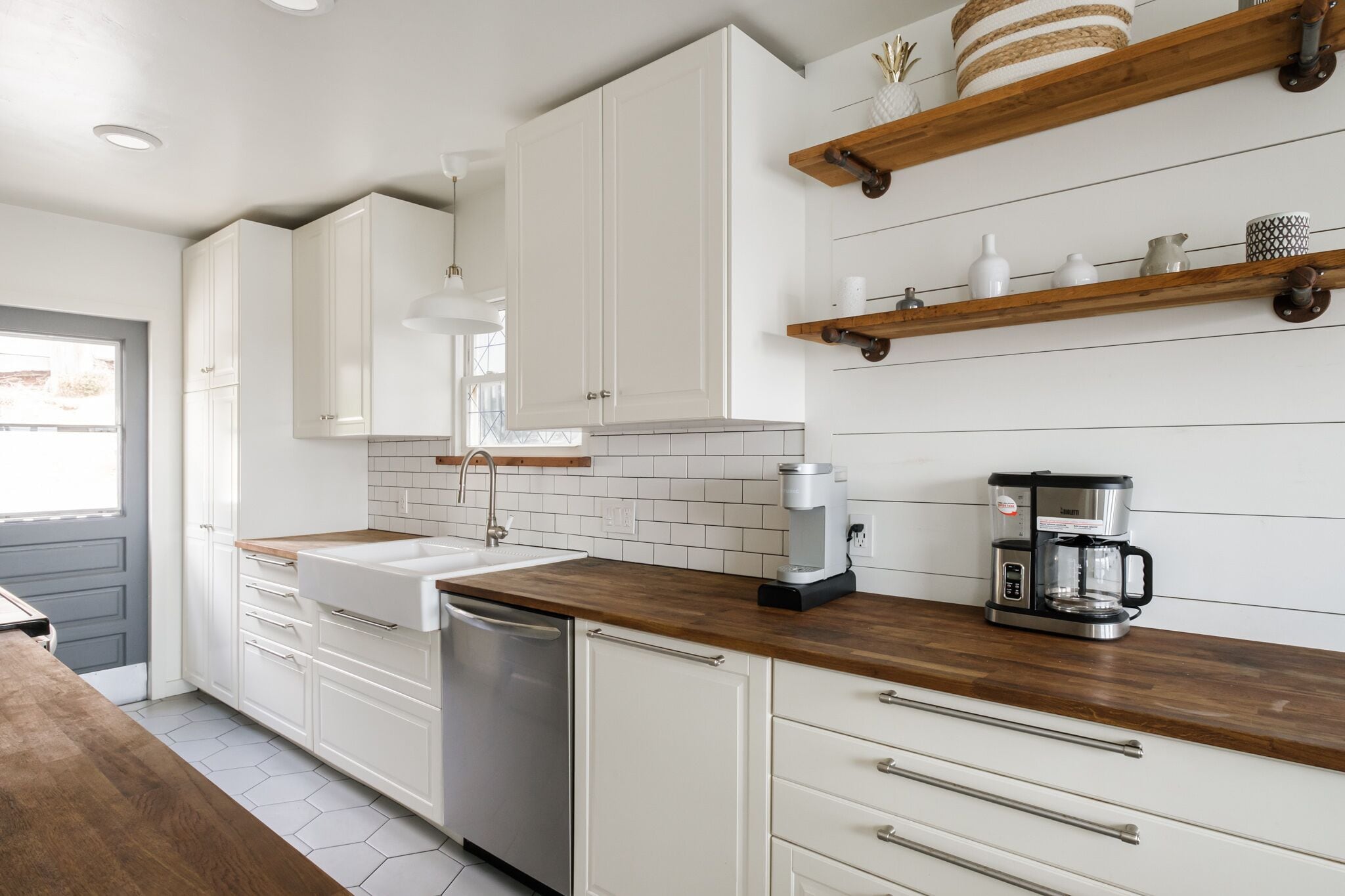 Een moderne keuken met witte kastjes, een houten aanrechtblad, een koffiezetapparaat en een vaatwasser.