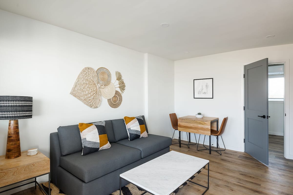 A modern living room with a grey sofa, a coffee table, a dining table with chairs, and a lamp.