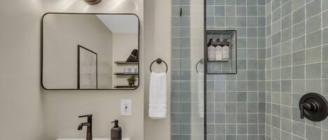 A modern bathroom with a rectangular sink, a mirror, a towel rack, and a shower area with a glass door.