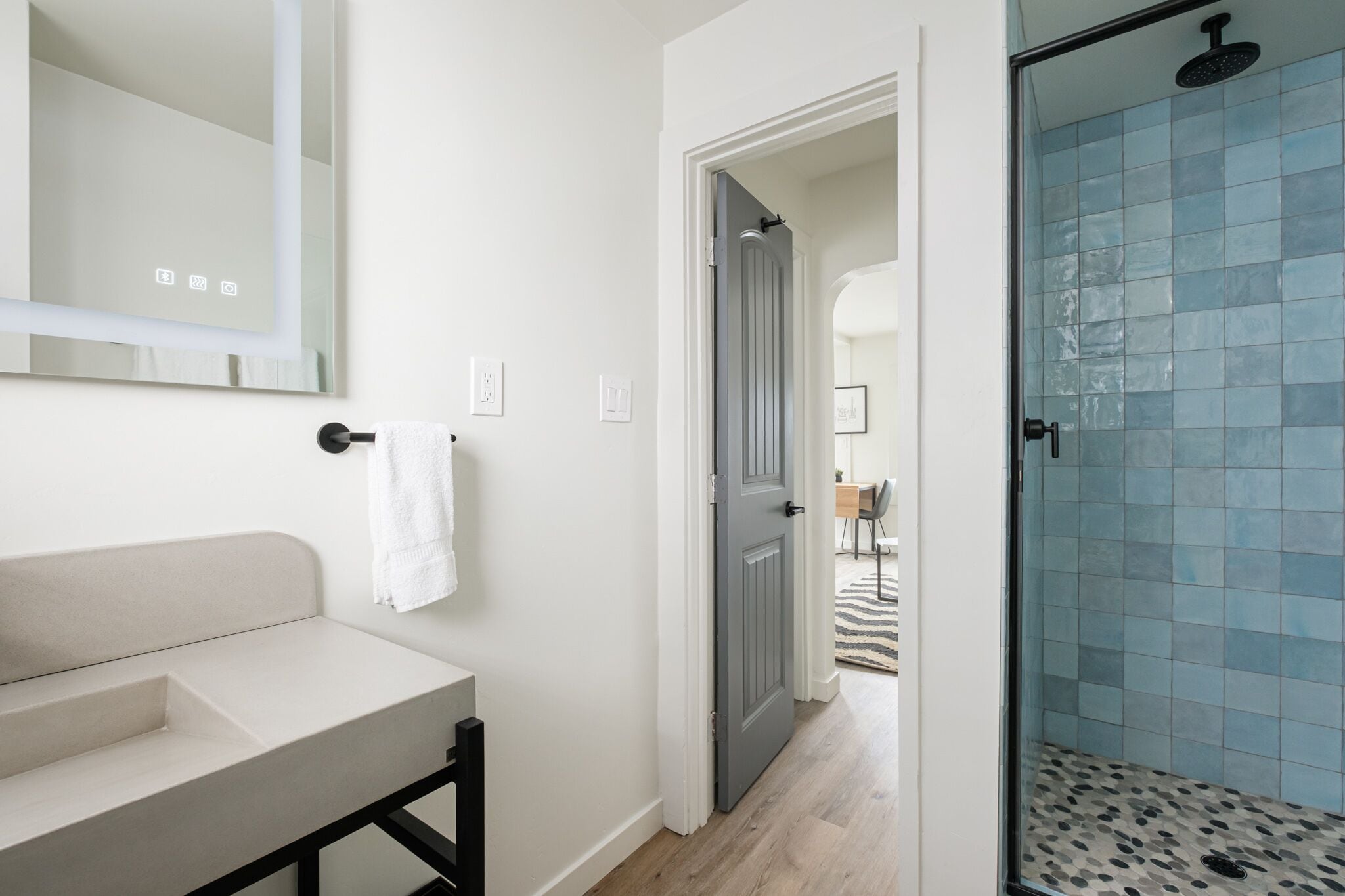 Een badkamer met een witte wastafel, een spiegel en een douche met blauwe tegels.