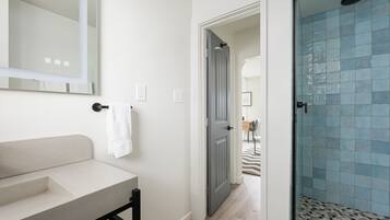 Een badkamer met een witte wastafel, een spiegel en een douche met blauwe tegels.