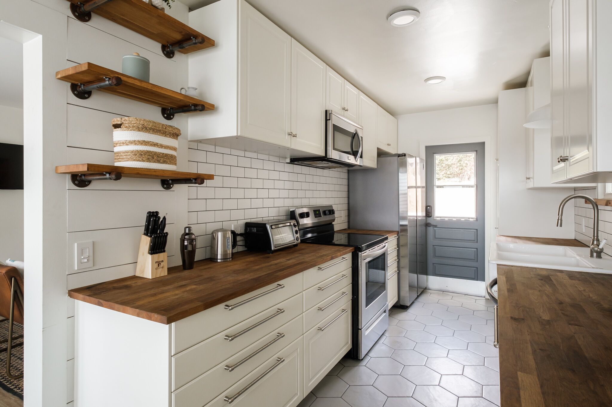 Una cocina moderna con armarios blancos, encimeras de madera, microondas, tostadora y refrigerador.