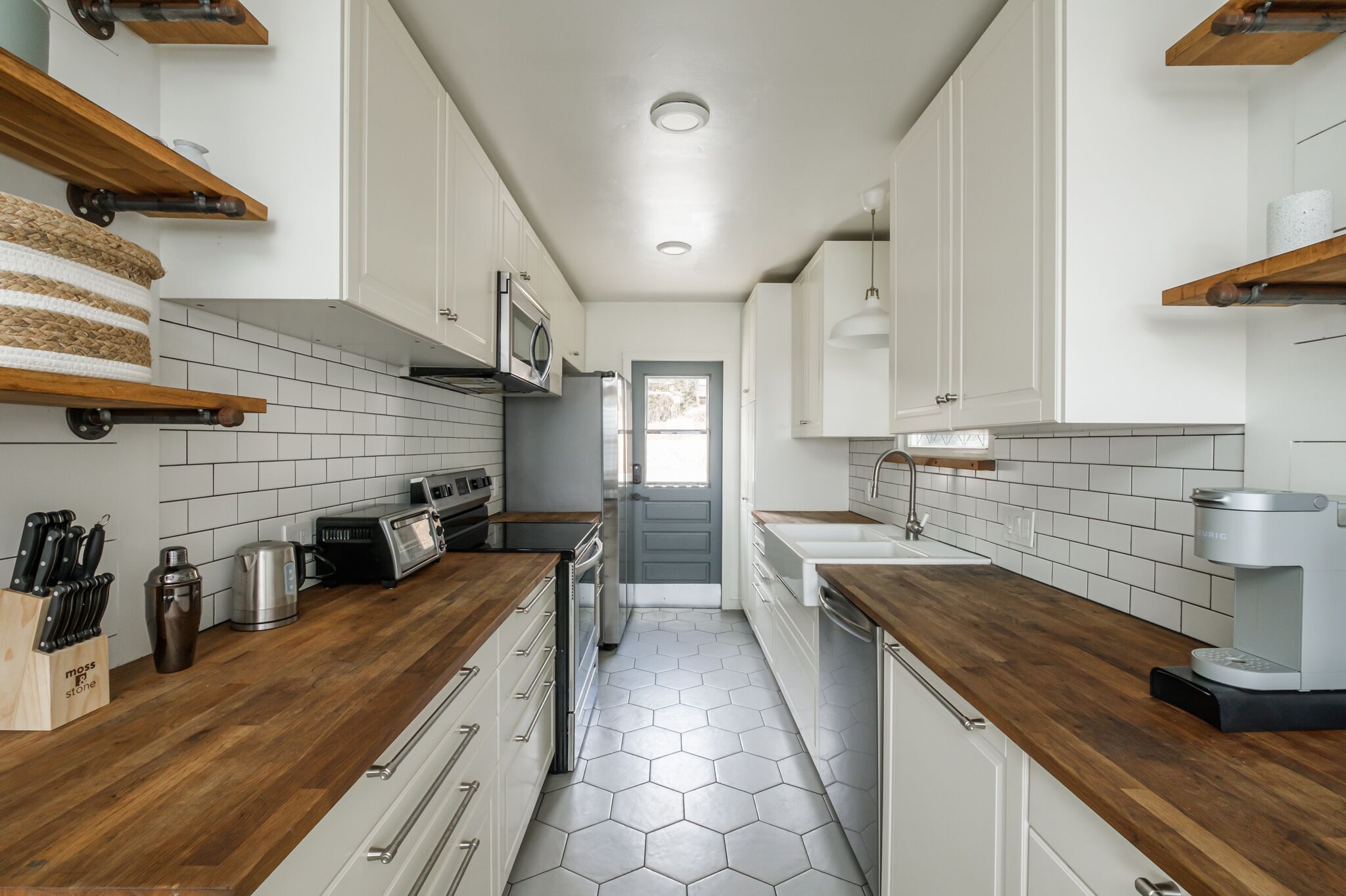 A narrow kitchen with white cabinets, wooden countertops, and a hexagonal tile floor.