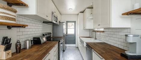 A narrow kitchen with white cabinets, wooden countertops, and a hexagonal tile floor.