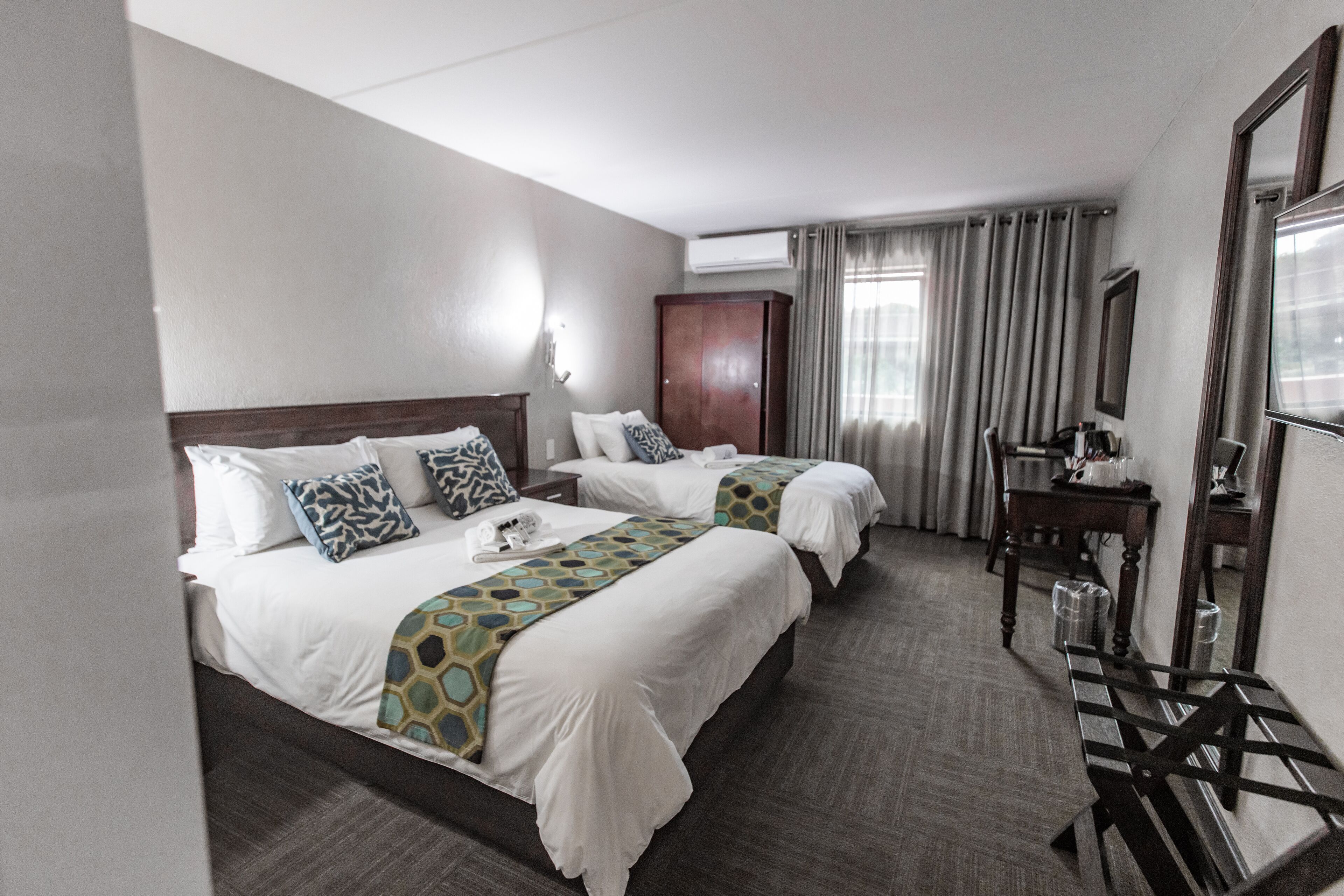 A hotel room with two beds, a desk, a chair, and a large mirror.