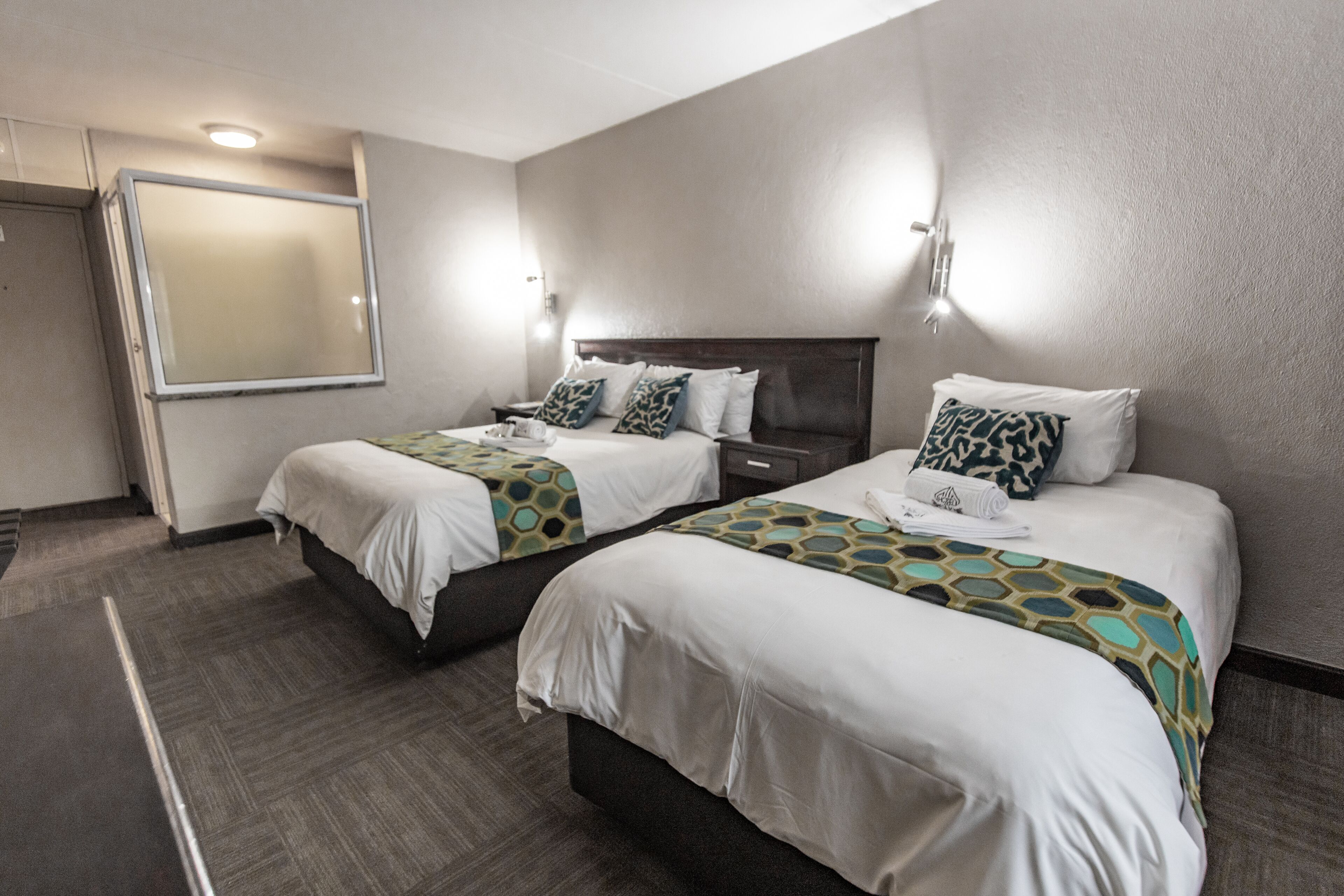 A hotel room with two beds, a large mirror, and wall-mounted lights.