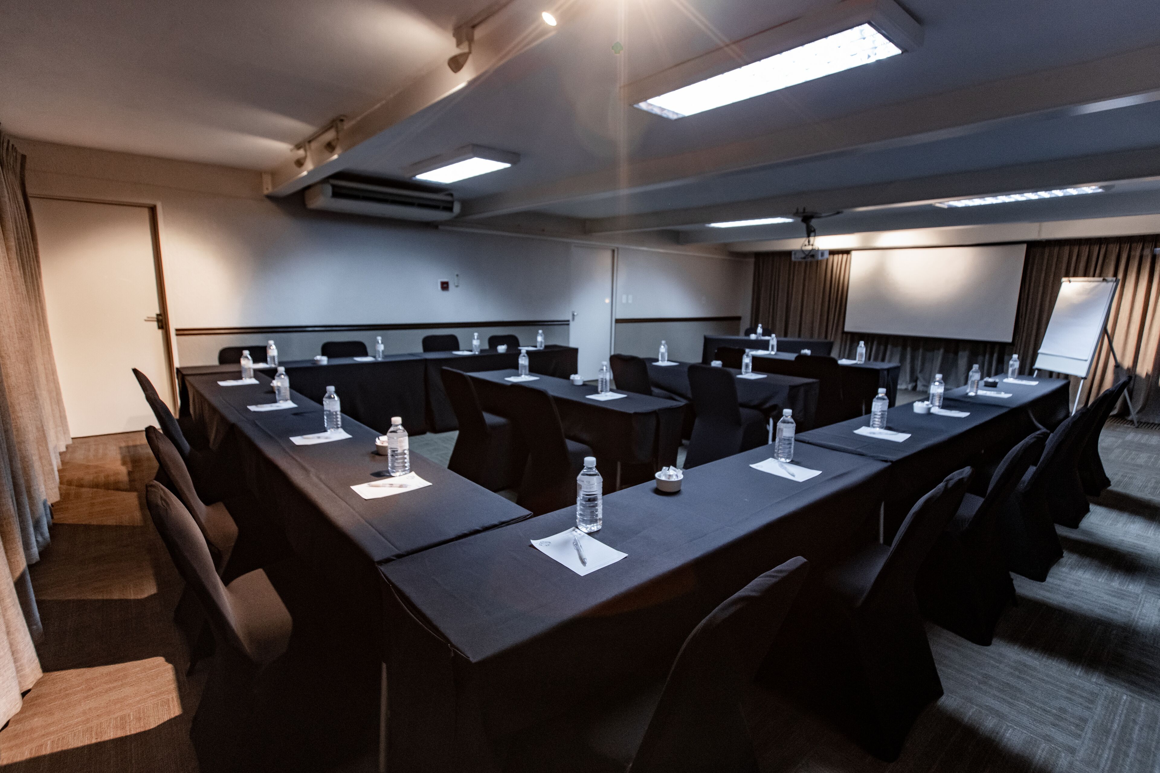 Une salle de conférence équipée de longues tables, de chaises et d’un écran de projection.