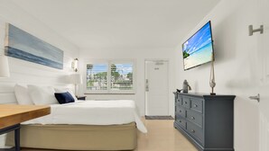 Ein Schlafzimmer mit einem Bett, einer Kommode, einem an der Wand befestigten Fernseher und einem Fenster mit Jalousien.