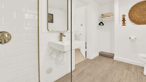 Un baño moderno con azulejos blancos tipo metro, un espejo con marco dorado, un lavamanos blanco y suelo de madera.