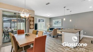 Een moderne keuken met een centraal eiland, een eetgedeelte met een houten tafel en stoelen, en een groot raam dat voor natuurlijk licht zorgt.