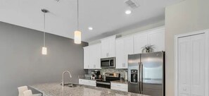 Eine moderne Küche mit weißen Schränken, Granit Arbeitsplatten, Edelstahlgeräten und einer Bar mit weißen Hocker.