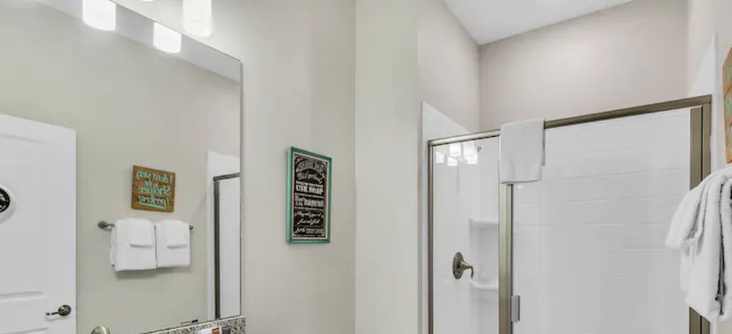 A bathroom with a granite countertop sink, a white toilet, a glass shower enclosure, and a mirror with two towels hanging on the wall.