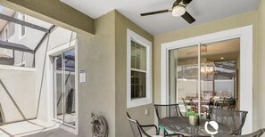 Ein überdachter Patio-Bereich mit Tisch und Stühlen, einem Deckenventilator und Blick in den angrenzenden Raum.