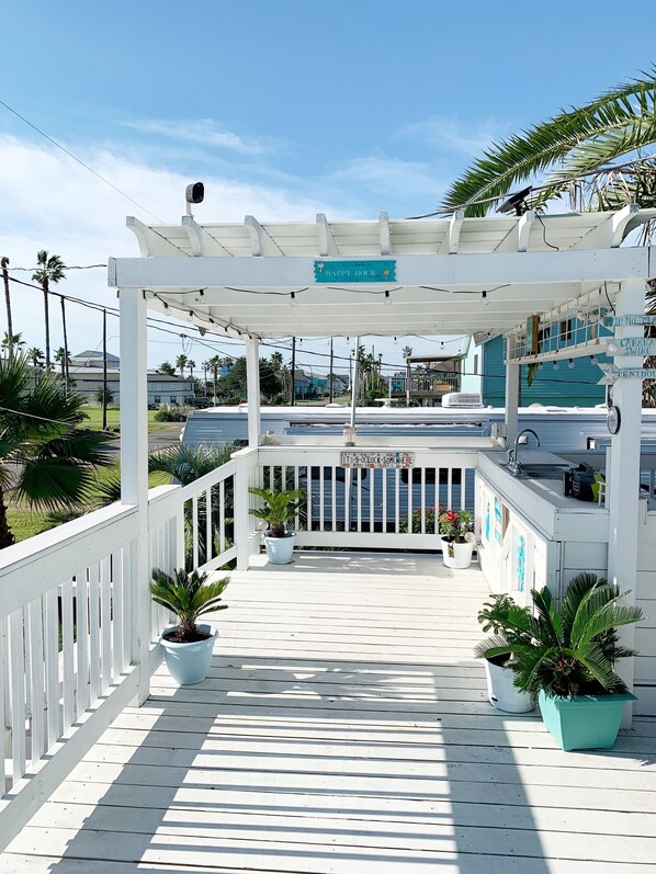 A covered outdoor area with a white railing, potted plants, and directional signs. - View of the bay (san leon)