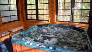 Una cabaña de madera con jacuzzi, bancos de madera y ventanas amplias.