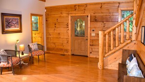 Un interior de madera con una escalera, una puerta con panel de vidrio y dos sillones con cojines estampados.