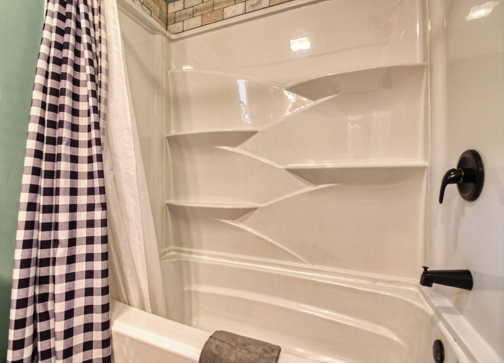 Una bañera con una cortina de ducha a cuadros, un revestimiento de azulejos en la pared de la ducha y un pomo de puerta negro.
