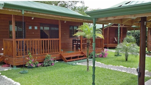 Une cabane en bois avec une véranda, une petite table et des chaises, et un jardin agrémenté de fleurs et de plantes.
