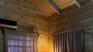 Une pièce chaleureuse aux murs en bois, avec un lit recouvert d’une couvre-lit à motifs, une lampe et des rideaux.
