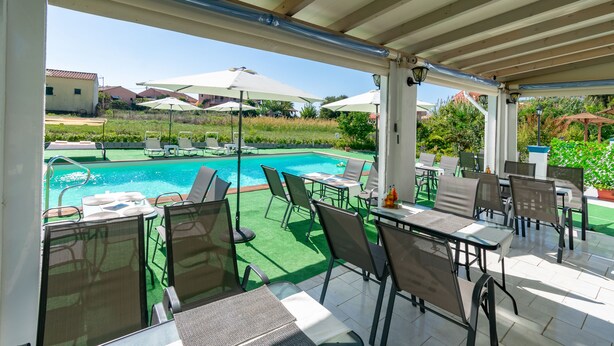 A covered outdoor area with a pool, chairs, tables, and umbrellas. - Akis Villa Studios & Apartments with Pool (Corfu)