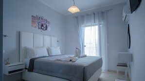 A modern bedroom with a large bed, a bedside table, a chair, and a window with curtains. - Akis Villa Studios & Apartments with Pool (Corfu)
