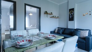 A dining area with a table set for four, white chairs, and a blue sofa in the background. - Akis Villa Studios & Apartments with Pool (Corfu)