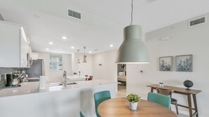 A modern kitchen with white cabinets, a central island, and a dining area with teal chairs and a wooden table. - 2bd/2ba condo close to Disney, Storey Lake (Kissimmee)
