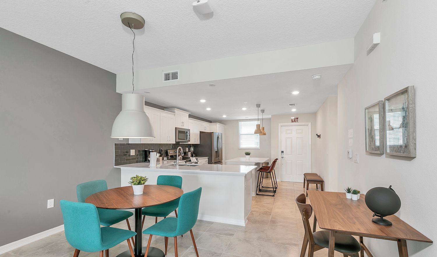 A modern kitchen with white cabinets, a central island, and a dining area with teal chairs and a wooden table.