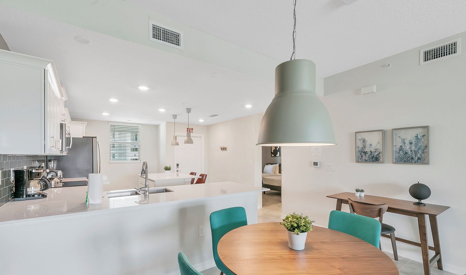 Une cuisine moderne avec des meubles blancs, un îlot central et un coin repas agrémenté de chaises turquoise et d’une table en bois.