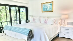 A bedroom with a large bed, a bedside table with a lamp, a sofa, and a view of greenery through the window. - Beach Condo located in the Heart of Olde Naples (Naples)