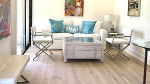 A modern living room with a white sofa, blue and white cushions, a glass coffee table, and a ceiling fan. - Beach Condo located in the Heart of Olde Naples (Naples)