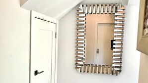 A hallway with a white door, a fluffy white bench, and a wall-mounted mirror with a geometric frame. - Beach Condo located in the Heart of Olde Naples (Naples)