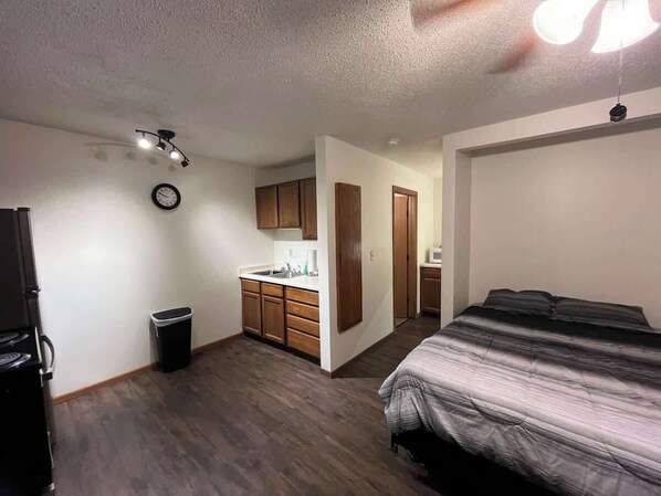 A compact room with a kitchenette, a bed, and a small bathroom.