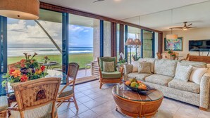 A spacious living room with a large window overlooking the ocean, furnished with a sofa, chairs, and a coffee table. - Oceanfront 1bd condo with endless ocean views (Lahaina)