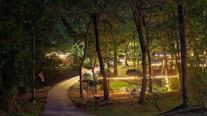 A nighttime view of a forested area with a paved path leading to a building with string lights. - Peggers Luxury Tiny Cabin at Lookout - Loaded (Chattanooga)