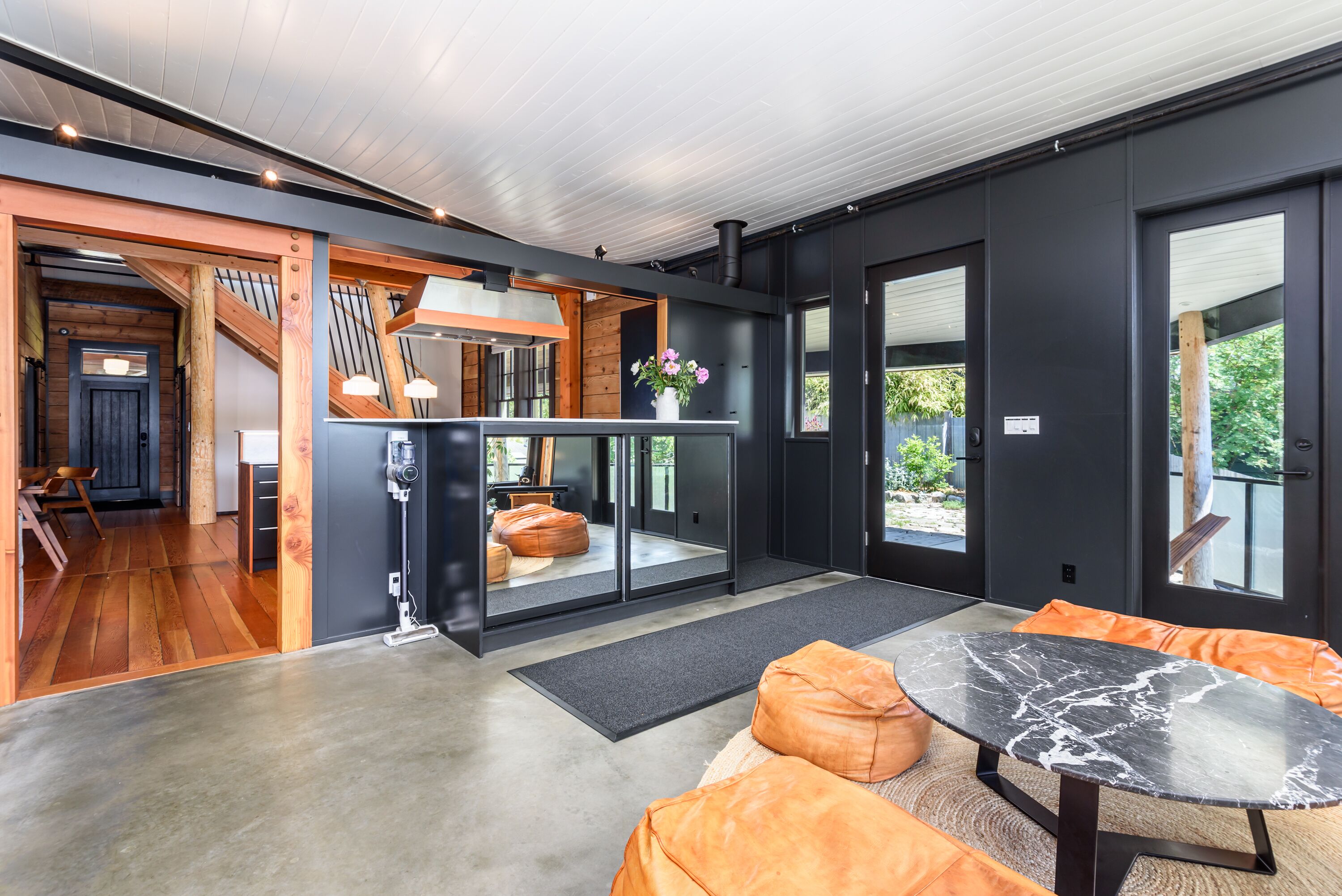 Une cuisine moderne avec un plafond en bois, un coin repas doté d’une table en marbre et un espace détente avec des coussins orange.