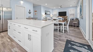 Una cocina moderna con armarios blancos, una isla central y una zona de comedor con mesa y sillas de madera.