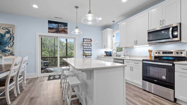 Cocina moderna con armarios blancos, una isla central, electrodomésticos de acero inoxidable y un comedor con sillas de madera.