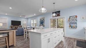 Una cocina amplia con una isla central, armarios blancos y una zona de comedor con un sofá azul.