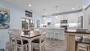 Una cocina moderna con armarios blancos, una isla central y un comedor con mesa y sillas de madera.